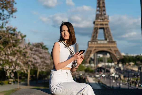 在法国巴黎埃菲尔铁塔附近 身穿时髦服装的年轻貌美的女人坐在智能手机前 — 图库照片