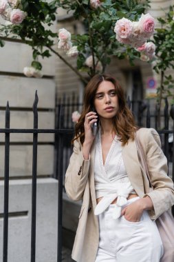 Şık bir kadın akıllı telefonuyla konuşuyor Fransa 'da şehir sokağında çiçek açan güllerin yanında 