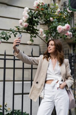 Şık bir kadın akıllı telefonuyla selfie çekiyor. Paris 'te çiçek açan güllerin yanında. 