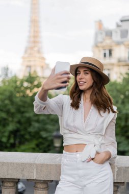 Gülümseyen turist, Paris 'te Eyfel Kulesi' nin arka planında akıllı telefonuyla selfie çekiyor. 