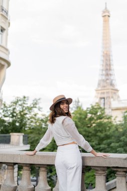 Hasır şapkalı neşeli gezgin Fransa 'da arka planda Eyfel kulesi olan kameraya bakıyor. 
