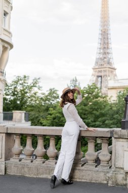 Güneş şapkalı mutlu genç kadın Paris 'te arka planda Eyfel kulesiyle kameraya bakıyor. 