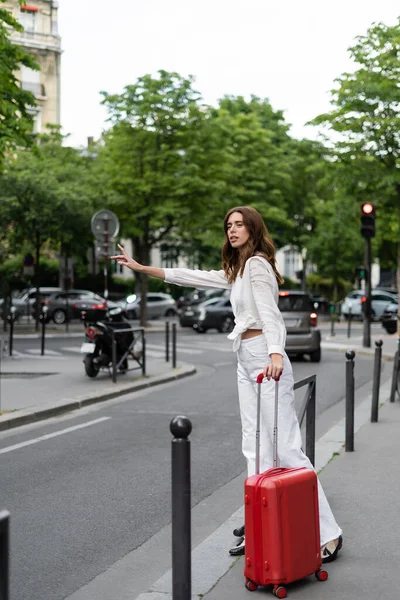 パリの都会の通りに近い道路にスーツケースキャッチタクシーでスタイリッシュな旅行者 — ストック写真