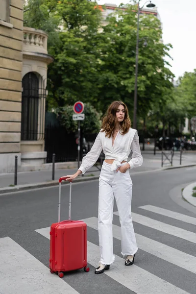 Fashionable woman with suitcase walking on urban street in Paris