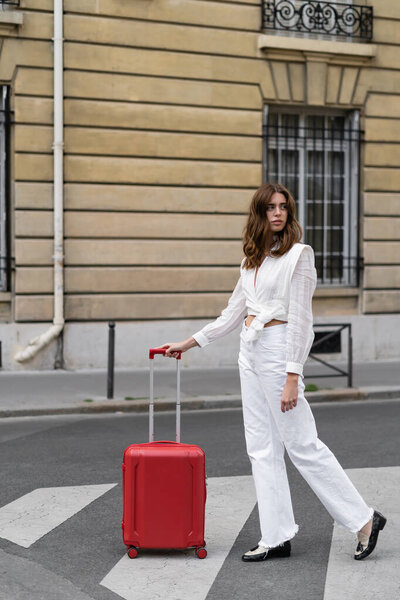 Young woman in blouse standing near suitcase on urban street in France 