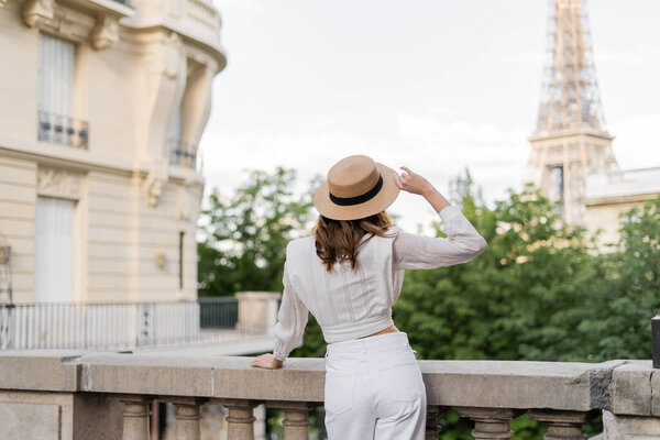 Back view of stylish woman holding sun hat with Eiffel tower at background in Paris 