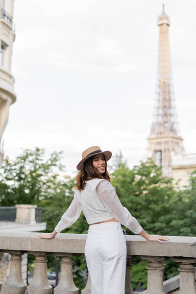 Cheerful traveler in straw hat looking t camera with Eiffel tower at background in France 