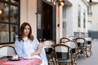 Esmer kadın Paris 'teki açık kafede kahve ve tatlıya yakın bir yerde kameraya bakıyor. 