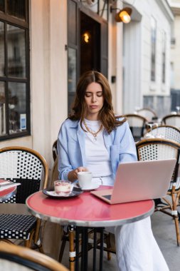 Freelancer, tatlıya yakın kahve fincanı ve dizüstü bilgisayarını Paris 'teki kafe masasında tutuyor. 