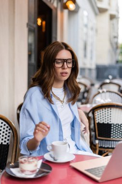 Paris 'teki kafe terasında kahve ve tatlının yanında bulanık dizüstü bilgisayara bakan şık bir kadın. 