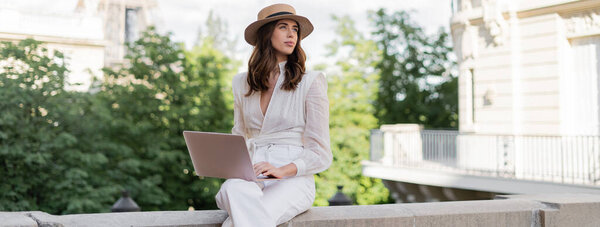 Freelancer in sun hat using laptop on urban street in Paris, banner 