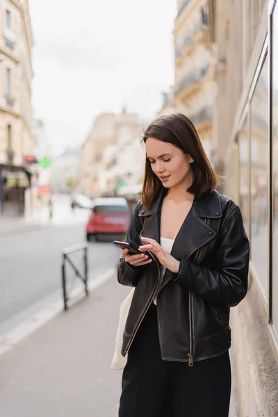 Jovem mulher em couro preto jaqueta mensagens no smartphone na rua em paris — Fotografia de Stock