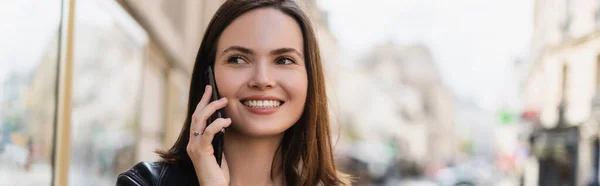 Jeune femme souriante en veste élégante parlant sur smartphone dans la rue urbaine, bannière — Photo de stock
