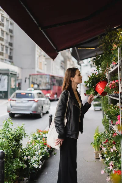 Вид збоку жінки з мішком для продавця полотен, який дивиться на зелені рослини з горщиками на вулиці в Парижі — стокове фото