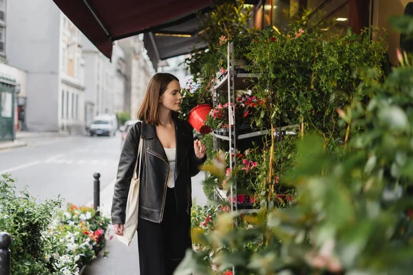 Jovem elegante com saco de lona shopper olhando para plantas envasadas verdes na rua em paris — Fotografia de Stock