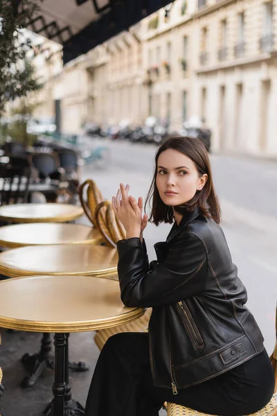 Stylish young woman in black leather jacket sitting in french cafe on summer terrace — Stock Photo
