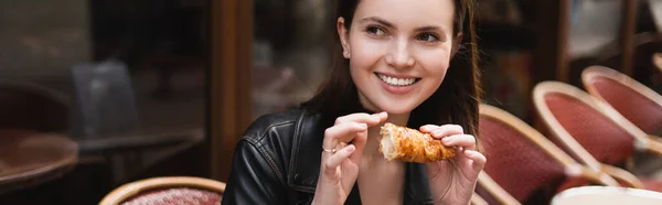 Mujer alegre sosteniendo croissant recién horneado en la cafetería al aire libre en París, bandera - foto de stock