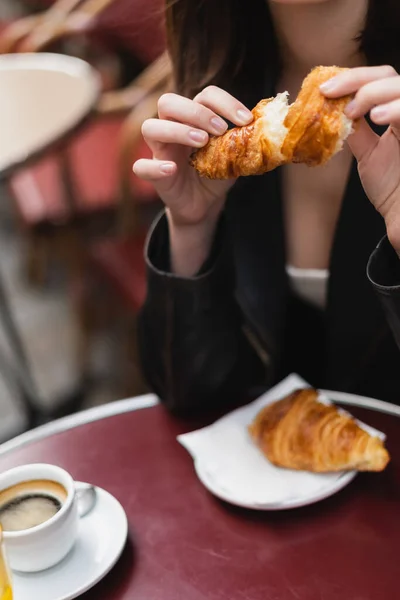 Vista recortada de la mujer sosteniendo croissant cerca de la taza de café en la cafetería al aire libre en París - foto de stock