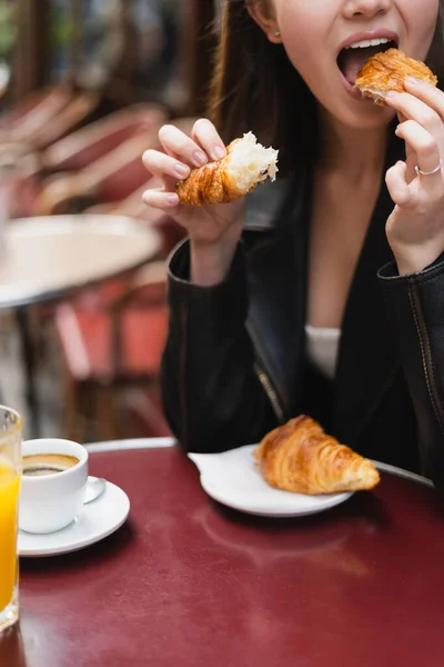 Vista recortada de la mujer comiendo croissant cerca de la taza de café y vaso de jugo de naranja en la cafetería al aire libre en París - foto de stock