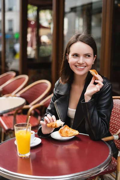 Positive Frau hält Croissant in der Nähe einer Tasse Kaffee und einem Glas Orangensaft in einem Café in Paris — Stockfoto