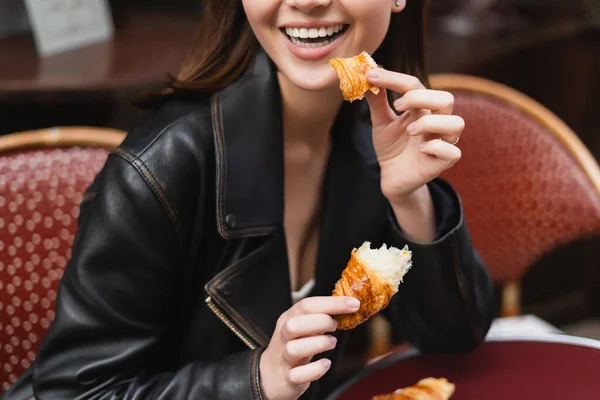 Vista parcial de la mujer feliz sosteniendo cruasán fresco en la cafetería al aire libre en París - foto de stock