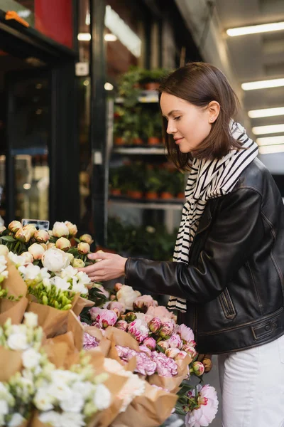 Vue latérale de la jeune femme en tenue élégante choisissant des fleurs dans la rue à Paris — Photo de stock