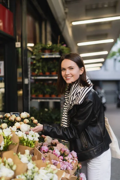 Mujer joven feliz en traje elegante elegir flores en la calle en París - foto de stock