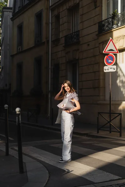 Молодая женщина в стильном наряде держит букет завернутый в бумагу на улице в Париже — стоковое фото