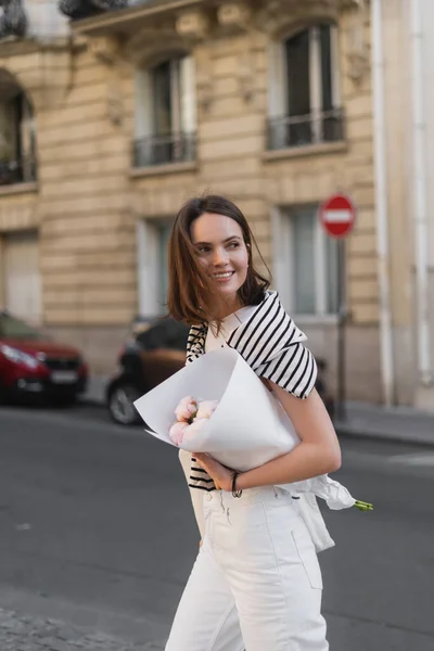 Giovane donna positiva in abito elegante con bouquet avvolto in carta su strada a Parigi — Foto stock