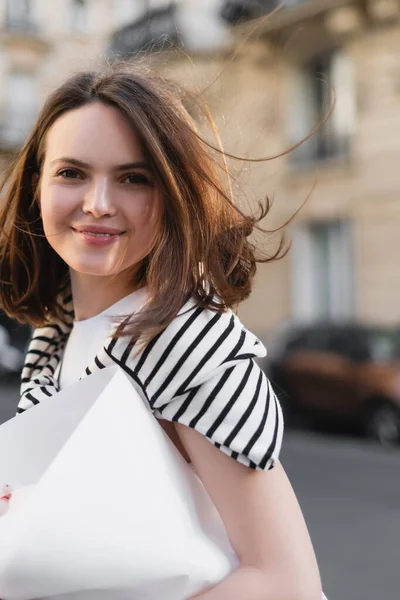 Mujer alegre en traje elegante celebración ramo envuelto en papel en la calle en París - foto de stock