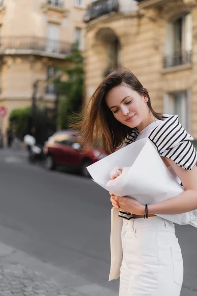 Giovane donna in abito alla moda con bouquet avvolto in carta su strada a Parigi — Foto stock