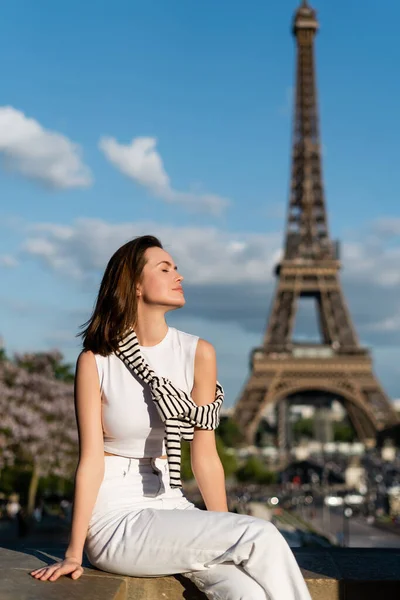 Молодая женщина в стильном наряде сидит рядом с Эйфелевой башней в Париже, Франция — стоковое фото