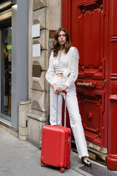 Donna bruna alla moda con valigia in piedi vicino alla valigia in strada urbana a Parigi — Foto stock