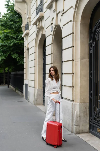 Donna alla moda in piedi vicino a valigia e edificio a Parigi — Foto stock