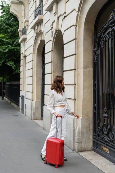 Seitenansicht einer brünetten Frau mit Koffer in der Nähe eines Gebäudes in Paris — Stockfoto