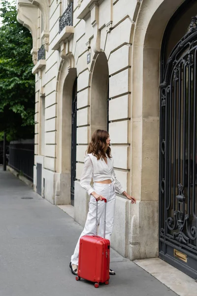 Vista lateral da mulher morena com mala perto do prédio em Paris — Fotografia de Stock