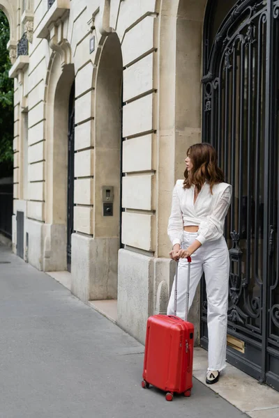 Side view of stylish brunette woman with baggage standing on urban street in Paris — Stock Photo
