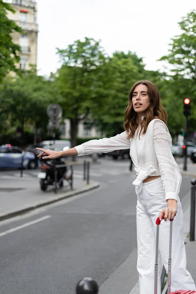 Turista con maleta coger un taxi cerca de la carretera en la calle en París - foto de stock