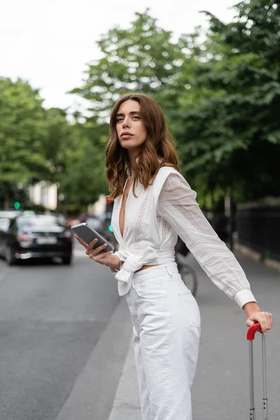 Trendy woman with mobile phone and suitcase on street in Paris — Stock Photo