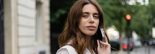 Брюнетка разговаривает по мобильному телефону на городской улице в Париже, баннер — стоковое фото