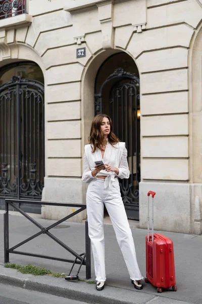 Donna alla moda in possesso di smartphone vicino al bagaglio in strada in Francia — Foto stock