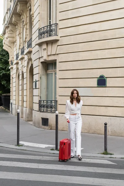 Стильний мандрівник з валізою, що йде на перехресті по вулиці в Парижі. — стокове фото