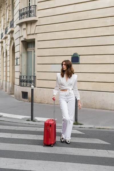 Fashionable traveler with suitcase walking on crosswalk on street in Paris — Stock Photo
