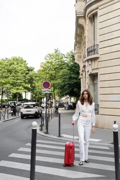 Brunette traveler with baggage walking on crosswalks on street in France — Stock Photo