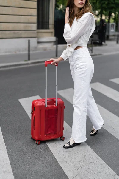 Обрезанный вид на стильную женщину с чемоданом, идущую по пешеходной дорожке в Париже — стоковое фото