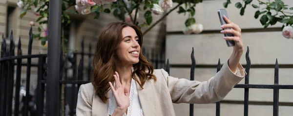 Smiling brunette woman having video chat on smartphone on urban street in France, banner — Stock Photo