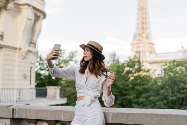 Tourist in sun hat taking selfie on cellphone with Eiffel tower at background in Paris — Stock Photo