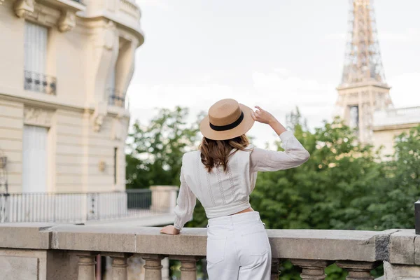 Back view of stylish woman holding sun hat with Eiffel tower at background in Paris — Stock Photo