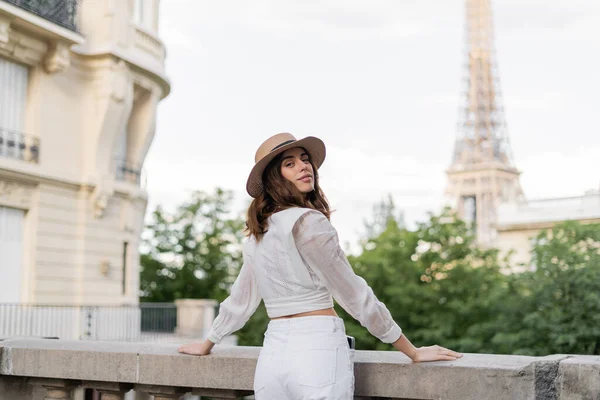 Mulher sorridente de chapéu de sol olhando para a câmera com torre Eiffel no fundo em Paris — Fotografia de Stock