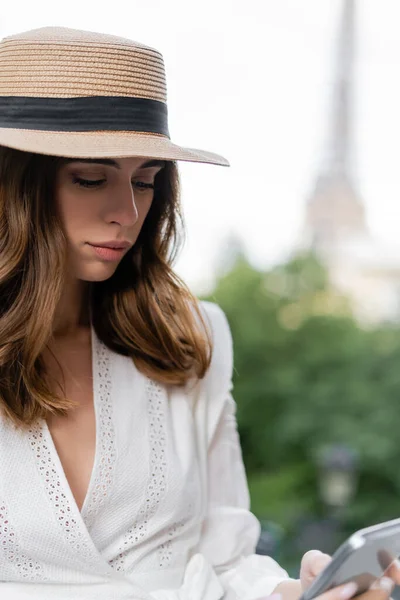 Стильная женщина в солнечной шляпе с помощью смартфона на улице в Париже — стоковое фото